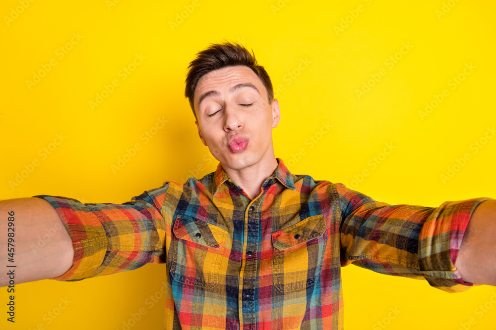 Self-portrait of attractive funny childish brown-haired guy sending air kiss isolated over bright yellow color background