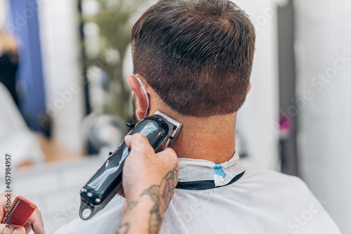 Barber cutting the hair of the nape of a man using an electric machine