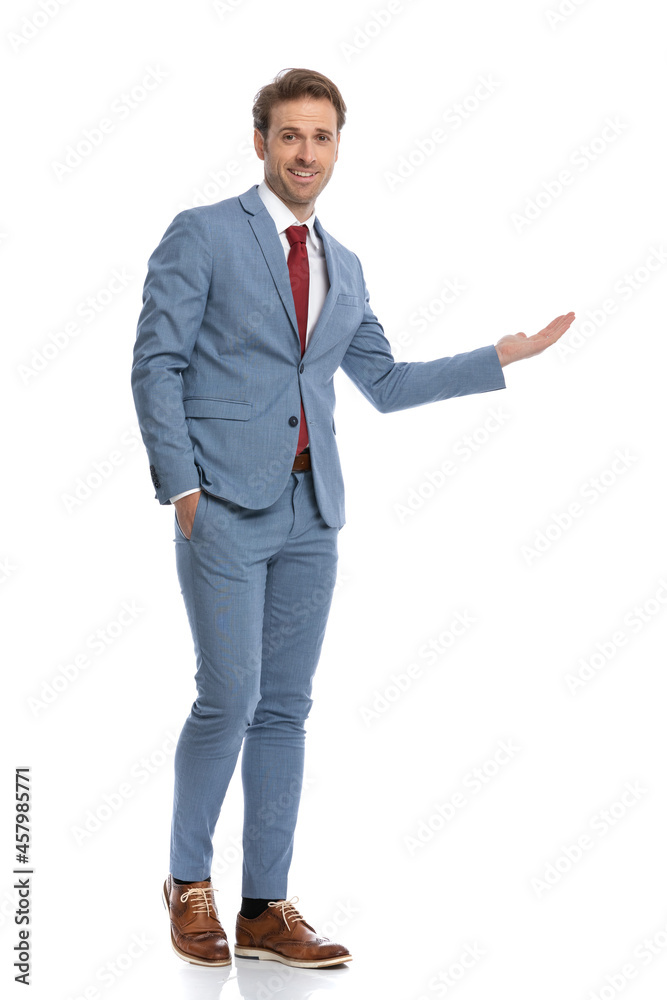 smiling young man in blue suit presenting to side and walking smiling young man in blue suit presenting to side and walking