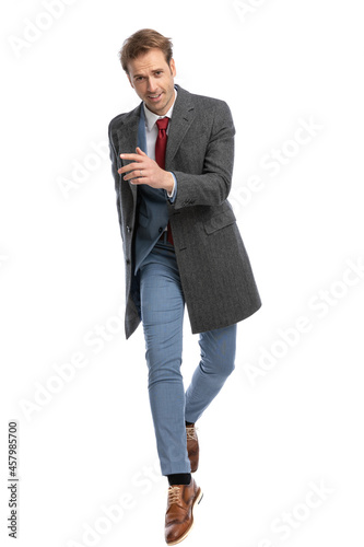 elegant businessman with grey coat holding arm in fashion pose and jumping