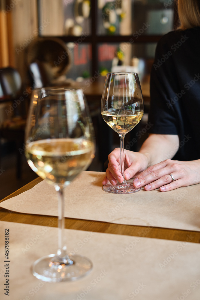 A glass of white wine in the hands of a girl relaxing in a restaurant. Tasting of alcoholic beverages. Summer rest. Romantic evening aperitif. Close-up of a glass of wine. Enjoy the moment