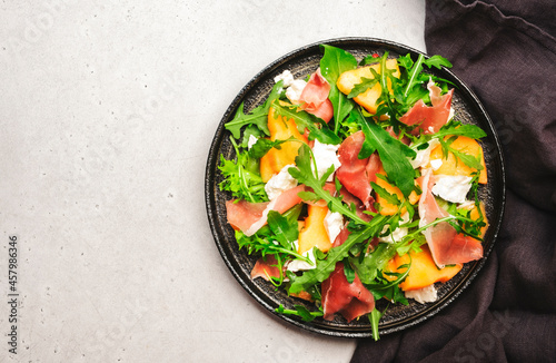 Melon salad with cantaloupe, prosciutto, goat cheese and arugula on white background, top view, copy space