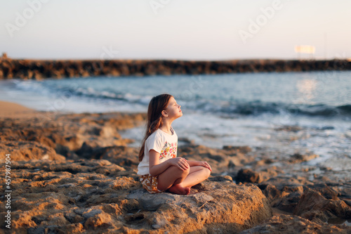 Cute caucasian child girl with long hair meditates by the sea, silence and calmness, warm toning