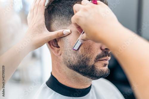 Hands of a hairdresser shaving a man with a razor