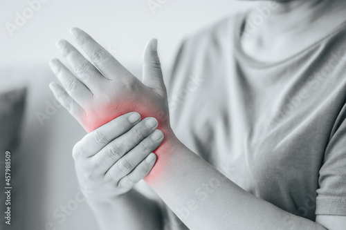 Closeup of woman sitting on sofa holds her wrist  hand injury with red highlight  feeling pain. Health care and medical concept.