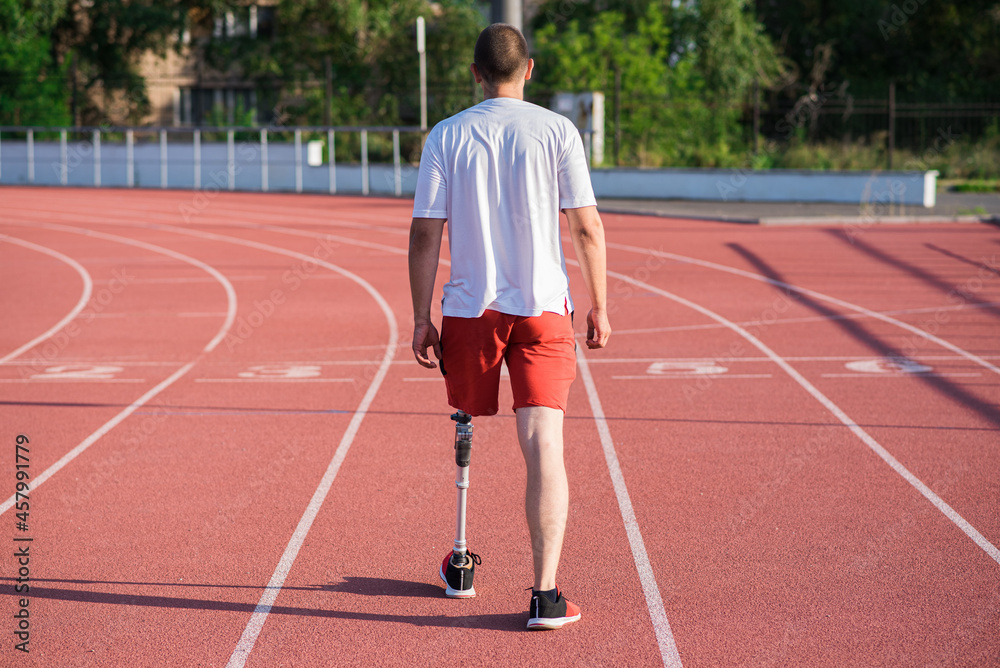 Obraz premium Caucasian male athlete with a prosthesis on his leg walking on the track at the stadium. Back view. Sport concept.
