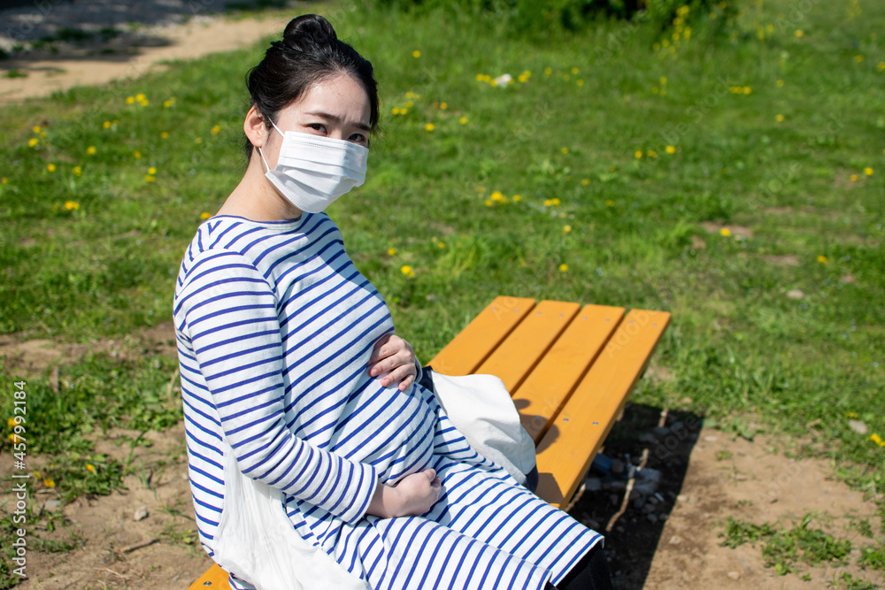 Fototapeta premium A young pregnant Asian woman sits on the outside bench and worries about her baby in her stomach