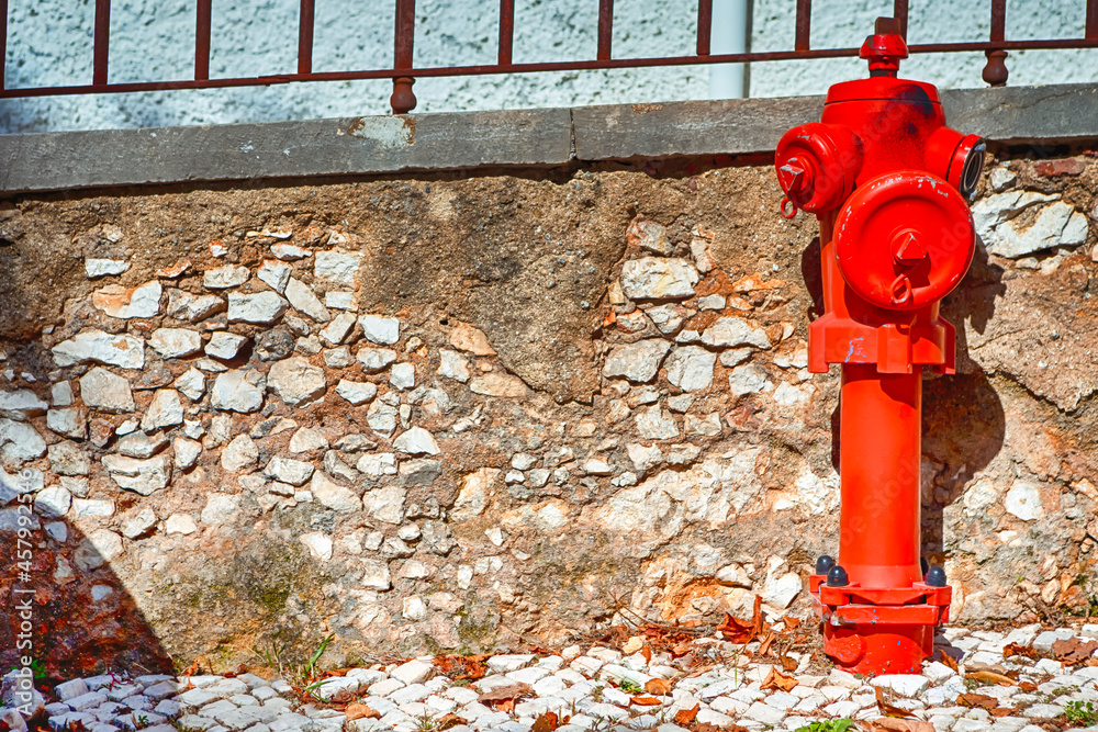 Closeup View of Old Styled Red Fire Cock Hydrant Against of Wall Located On One of The Streets in Portugal. Closeup View of Old Styled Red Fire Cock Hydrant Against of Wall Located On One of The Streets in Portugal.