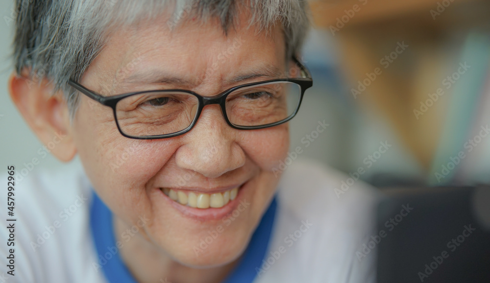 Gray hair woman face wears eyeglasses looking at blurry smartphone smiling. Happy modern granny using cellphone and wireless technology for video calling. Good looking senior female with spectacles