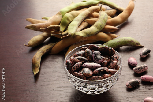 Photos Scarlet runner bean in a small crystal glass bowl on a dark surface with green and yellow hulls in a background