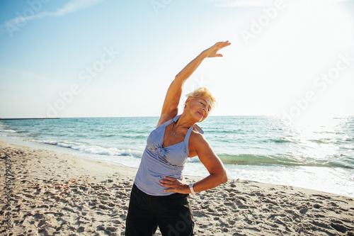 Fotografie Active senior woman stretching by the sea at sunrise