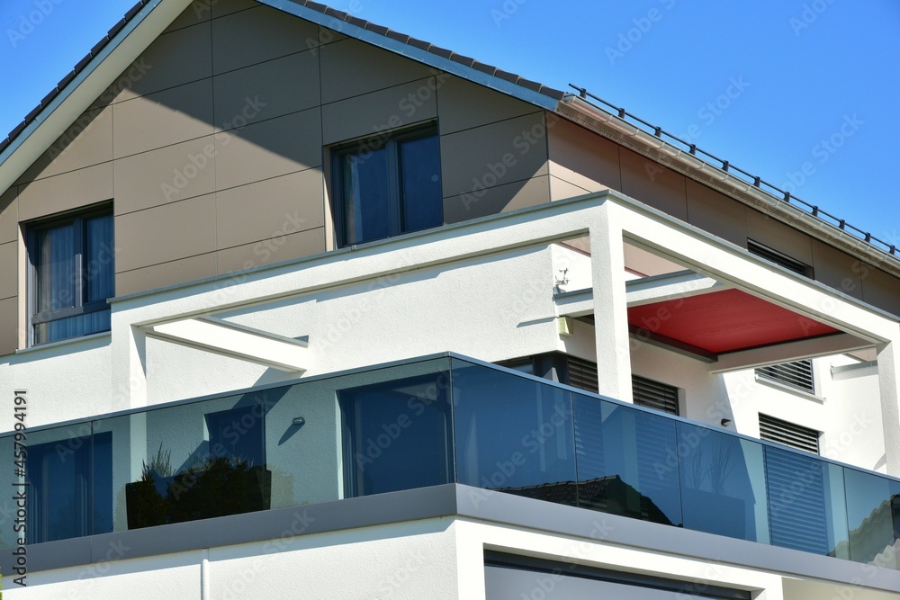 Integrierte Pergola mit Edelstahl-Attika als Sonnenschutz und Metallbalkon mit Rauchglas-Sichtschutz am mittleren Geschoss eines neu gebauten Einfamilienhauses