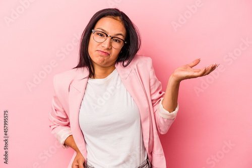 Young latin woman isolated on pink background  doubting and shrugging shoulders in questioning gesture.