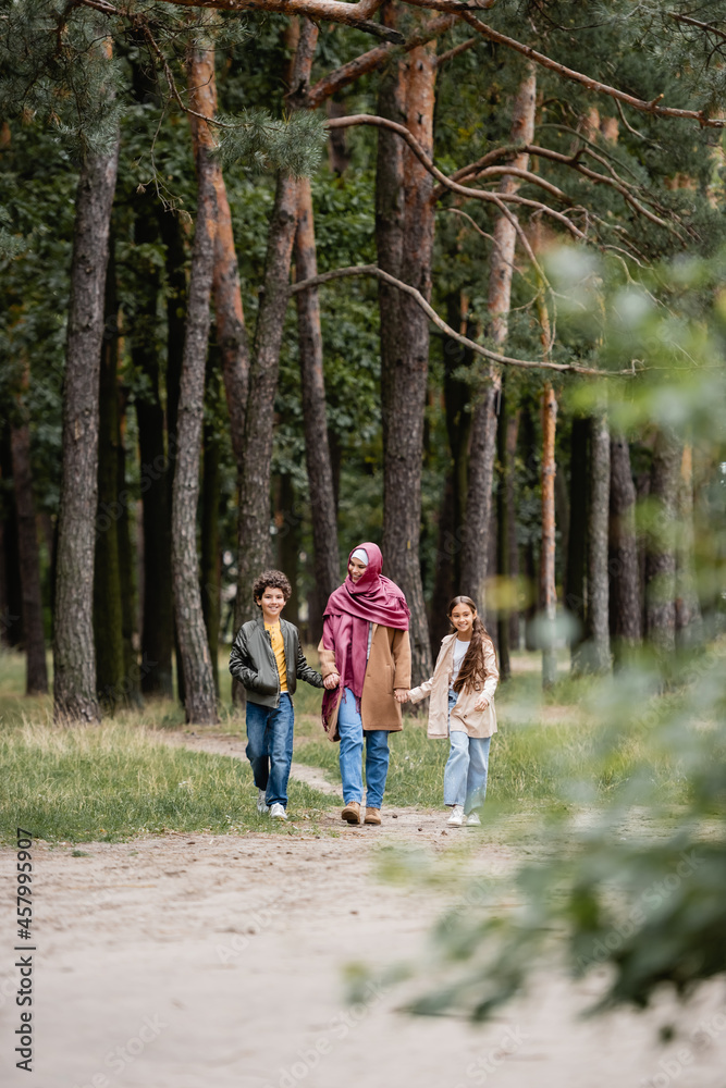 Fototapeta premium Arabian mother walking with kids in park during autumn