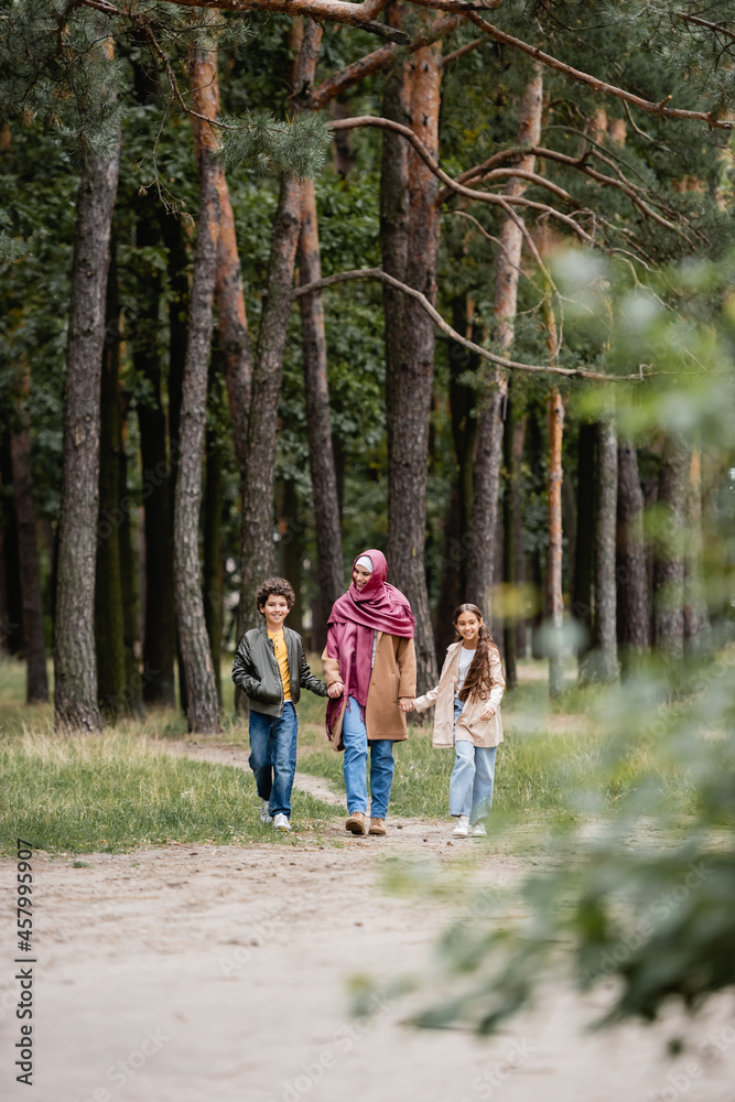 Arabian mother walking with kids in park during autumn