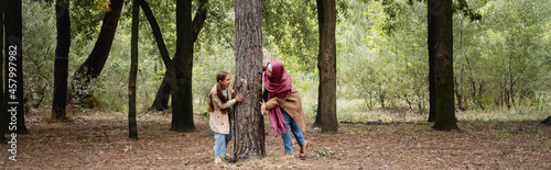 Smiling arabian girl playing with mother near tree in park, banner