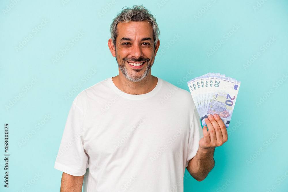 Middle age caucasian man holding bills isolated on blue background happy, smiling and cheerful. Middle age caucasian man holding bills isolated on blue background happy, smiling and cheerful.