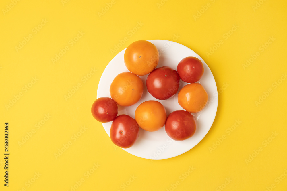Healthy food composition of various fresh yellow and red tomato isolated on a white plate on yellow background. Top view, banner. Healthy food composition of various fresh yellow and red tomato isolated on a white plate on yellow background. Top view, banner.