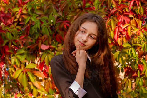 Schoolgirl in school clothes in nature on a background of autumn leaves. Girl 11 years old.