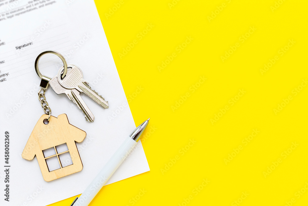 Keys with house shaped keychain and pen on real estate mortgage loan document, contract agreement to buy and construction new home, insurance, lease or rent apartments. Yellow background, copy space. Keys with house shaped keychain and pen on real estate mortgage loan document, contract agreement to buy and construction new home, insurance, lease or rent apartments. Yellow background, copy space.