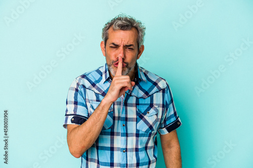 Middle age caucasian man isolated on blue background keeping a secret or asking for silence.