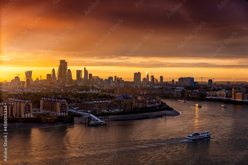 The skyline of London, United Kingdom, along the Thames river during a golden sunset with boat traffic