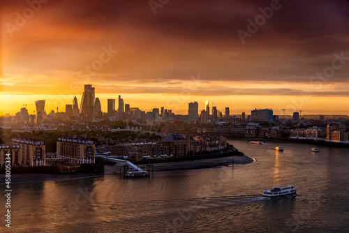 The skyline of London  United Kingdom  along the Thames river during a golden sunset with boat traffic