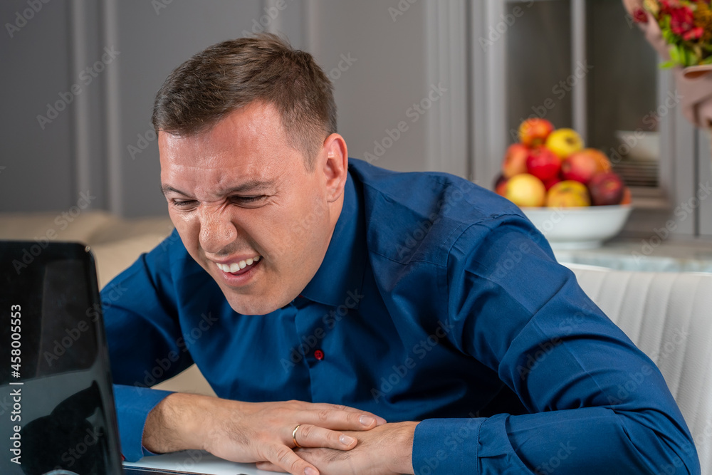 Man squints and tries see something small or reading suspicious message on laptop screen in living room at home. Confused millennial man reading news on laptop with disgust, unpleasant negative emotio Man squints and tries see something small or reading suspicious message on laptop screen in living room at home. Confused millennial man reading news on laptop with disgust, unpleasant negative emotio