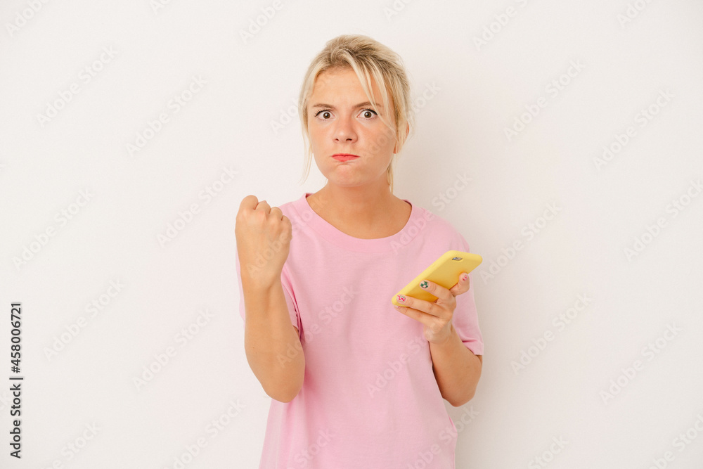 Young Russian woman holding mobile phone isolated on white background showing fist to camera, aggressive facial expression. Young Russian woman holding mobile phone isolated on white background showing fist to camera, aggressive facial expression.
