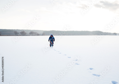 unrecognizable little boy in winter overalls walks alone in the snow, leaving traces. Winter active walks on freshly fallen snow. Frosty weather. © Anna
