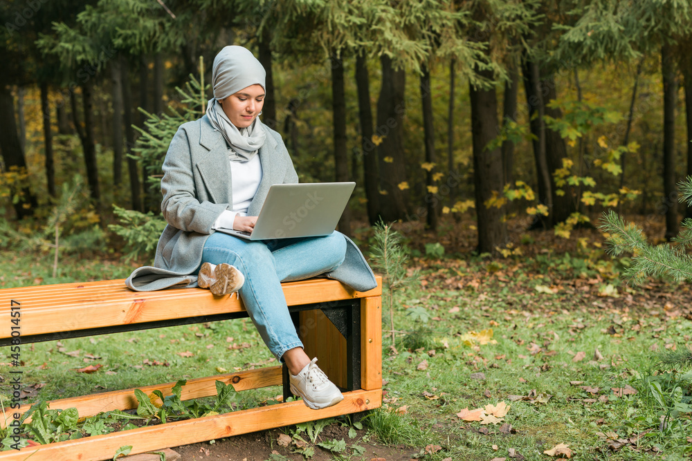 Fototapeta premium Young asian muslim woman using laptop at autumn park. Online education, online shopping and social networks concept.