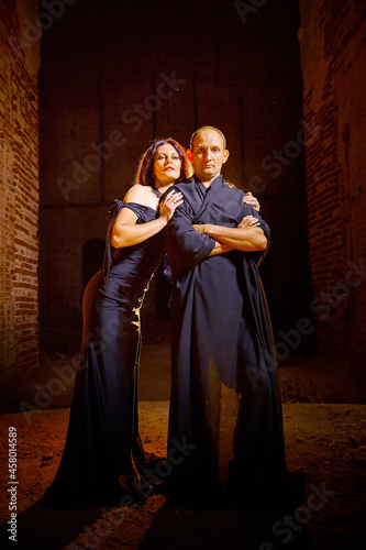 A couple in old dark clothes in an abandoned castle with old brick walls. A man and a woman posing in a dark gloomy mysterious dangerous hall. The evil king and Queen on Halloween