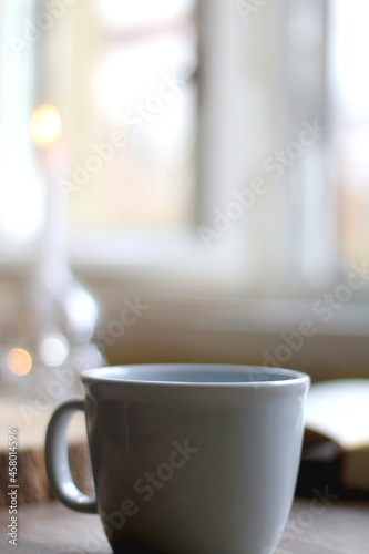 Bowl of cookies, cup of hot beverage, open book and lit candles on a table. Selective focus.