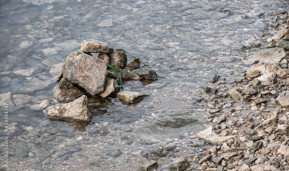 Fototapeta premium A pile of stones at the riverside. Transparent water with reflections and rocky banks. Rural landscapes by the water.