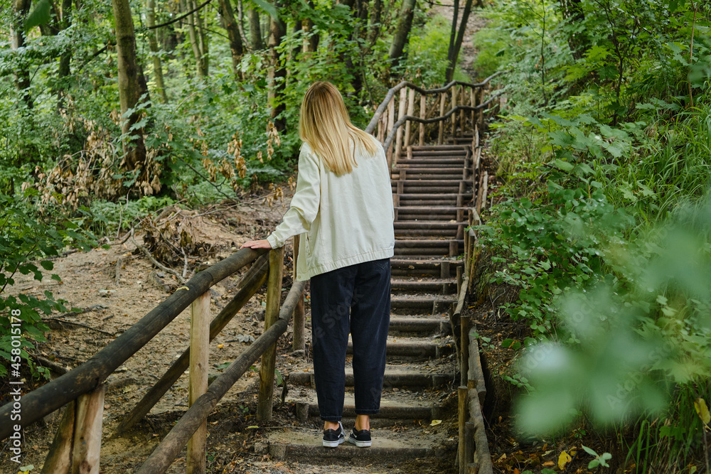 A woman climbs a wooden staircase in a picturesque park. Outdoor activities. Way up the stairs. Walk in nature. Enjoy the weather and fresh air. Weekend in nature A woman climbs a wooden staircase in a picturesque park. Outdoor activities. Way up the stairs. Walk in nature. Enjoy the weather and fresh air. Weekend in nature