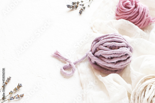 Pink and lilac skeins of thread for knitting and weaving on a white tablecloth.