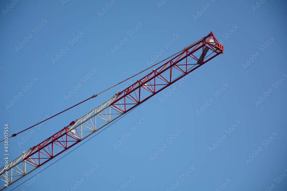 The crane jibs against blue sky. Construction site.