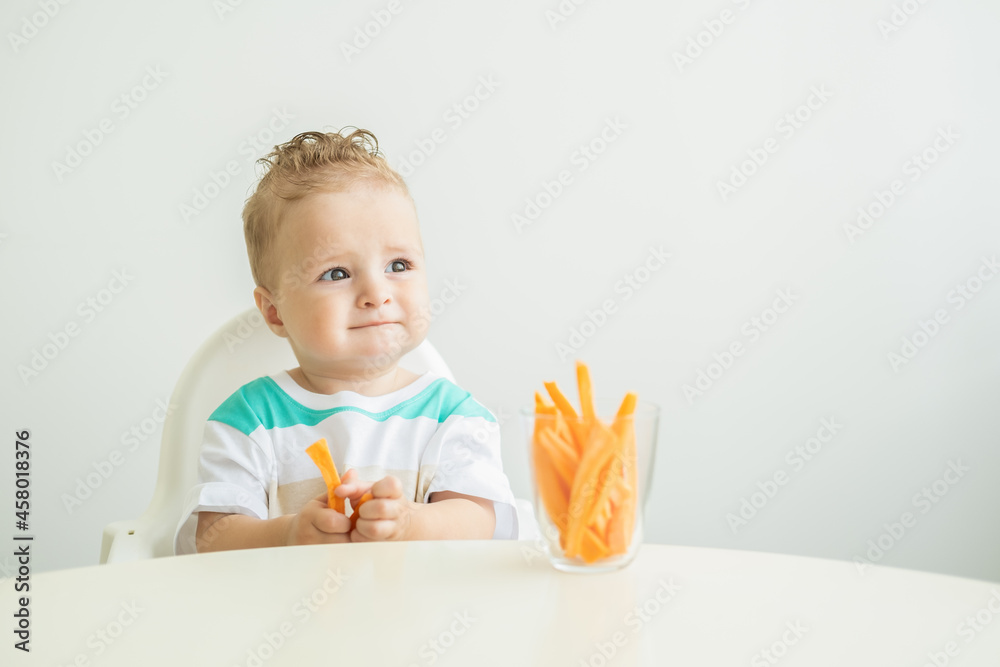 Baby boy sitting in a Childs chair eating carrot slices on white background. Baby boy sitting in a Childs chair eating carrot slices on white background.
