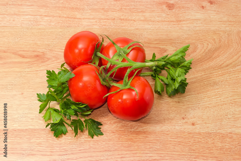 Branch of red tomatoes and parsley twigs on wooden surface