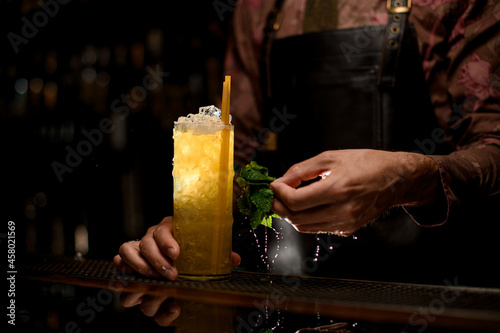 great view of glass full of ice and cocktail with drinking straws and male hand with wet mint leaves