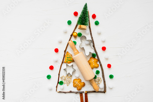 Abstrakt von einem Weihnachtsbaum mit einem Nudelholz und Backzutaten auf einem weißen Hintergrund. Draufsicht, bunt.