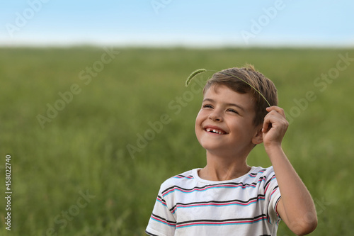 Cute little boy with spikelet in field, space for text. Child spending time in nature