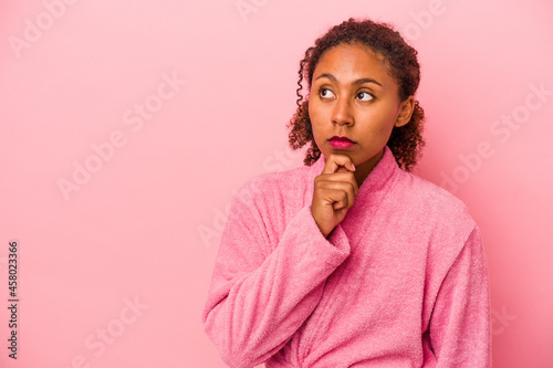 Young african american woman wearing a bathrobe isolated on pink background looking sideways with doubtful and skeptical expression.
