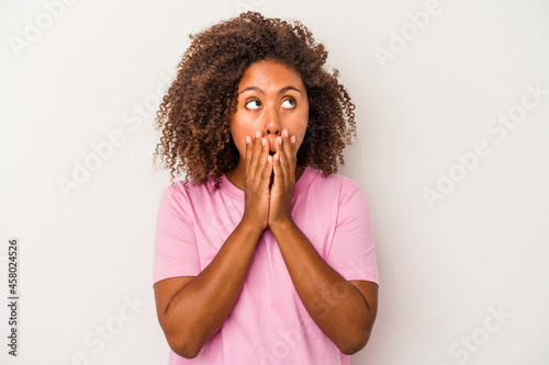Young african american woman with curly hair isolated on white background thoughtful looking to a copy space covering mouth with hand.