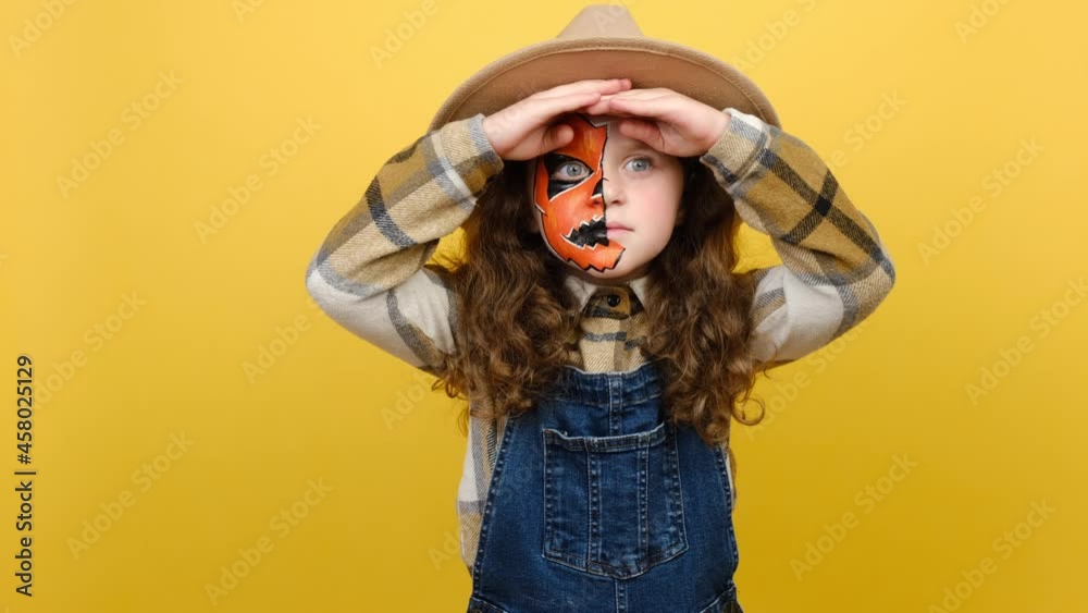 Portrait of cute attractive little girl child with Halloween mask looking far away inspecting horizon, holding hands over eyes peering distance, posing isolated over yellow studio background wall Portrait of cute attractive little girl child with Halloween mask looking far away inspecting horizon, holding hands over eyes peering distance, posing isolated over yellow studio background wall