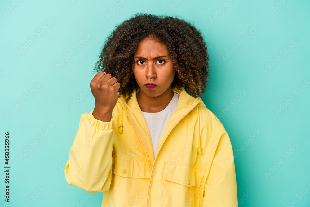 Young african american woman with curly hair isolated on blue background showing fist to camera, aggressive facial expression.