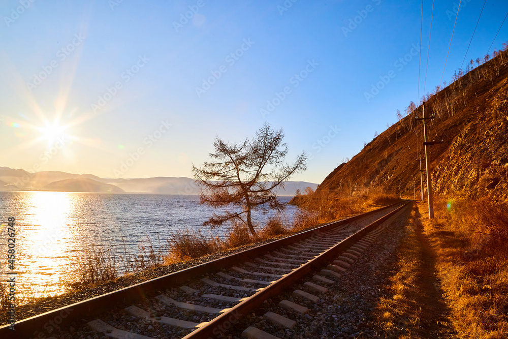 Obraz premium Circum Baikal railway running along the shore of Lake Baikal on an autumn sunny day with a yellow landscape around