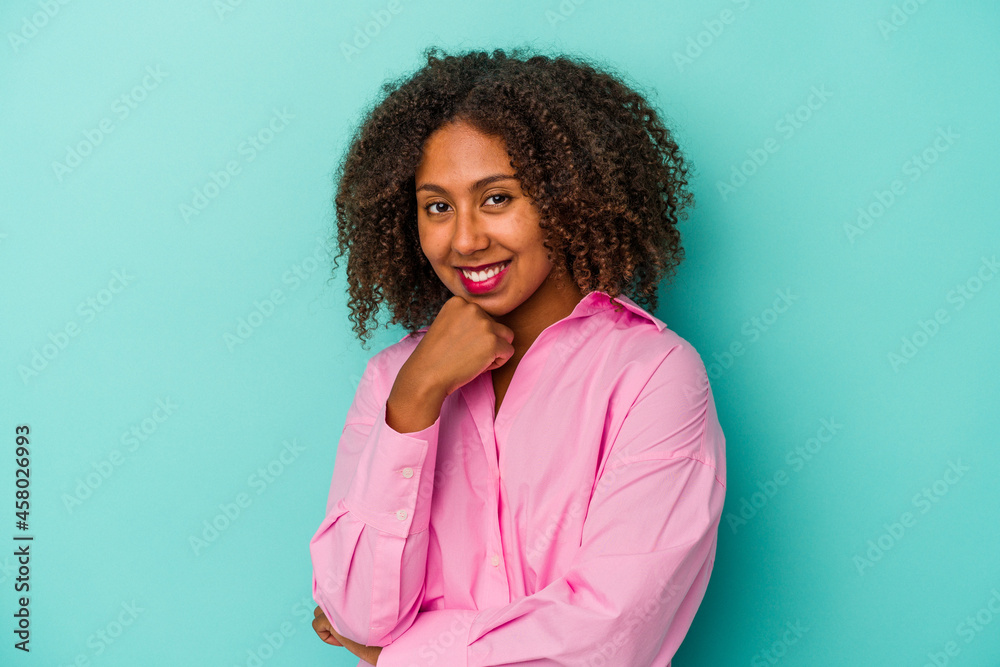 Young african american woman with curly hair isolated on blue background smiling happy and confident, touching chin with hand. Young african american woman with curly hair isolated on blue background smiling happy and confident, touching chin with hand.