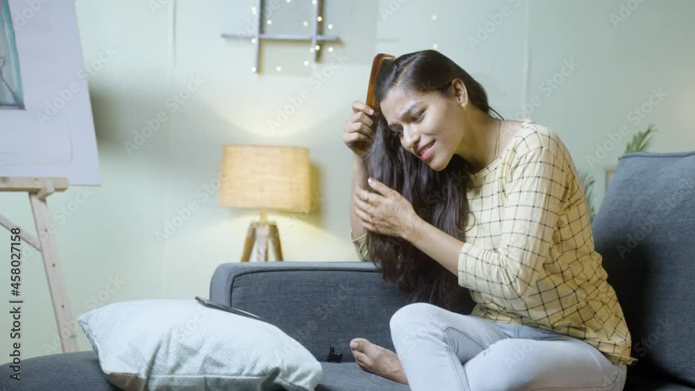 Young woman combing or hair styling by waching online tutorial or using social media in mobile phone - concept of haircare, beauty care and lifestyle Young woman combing or hair styling by waching online tutorial or using social media in mobile phone - concept of haircare, beauty care and lifestyle
