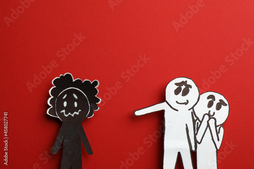 White paper figures mocking at black one on red background, flat lay. Racism concept photo